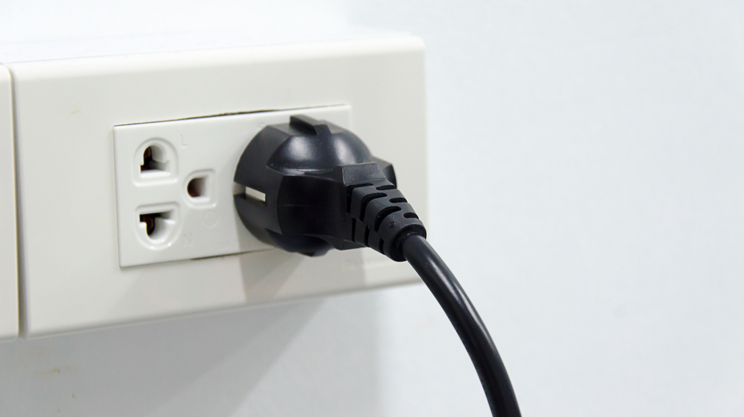 Black electrical plug connected to a white wall outlet
